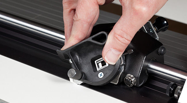 Hand on blade of mat cutter cutting into a white mat for framing a picture