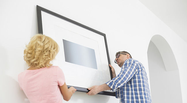 Man and woman hanging a framed piece on a wall
