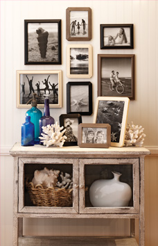 Decorative table decorated with seaside accents that has multiple photos framed in ready made frames hanging above it.
